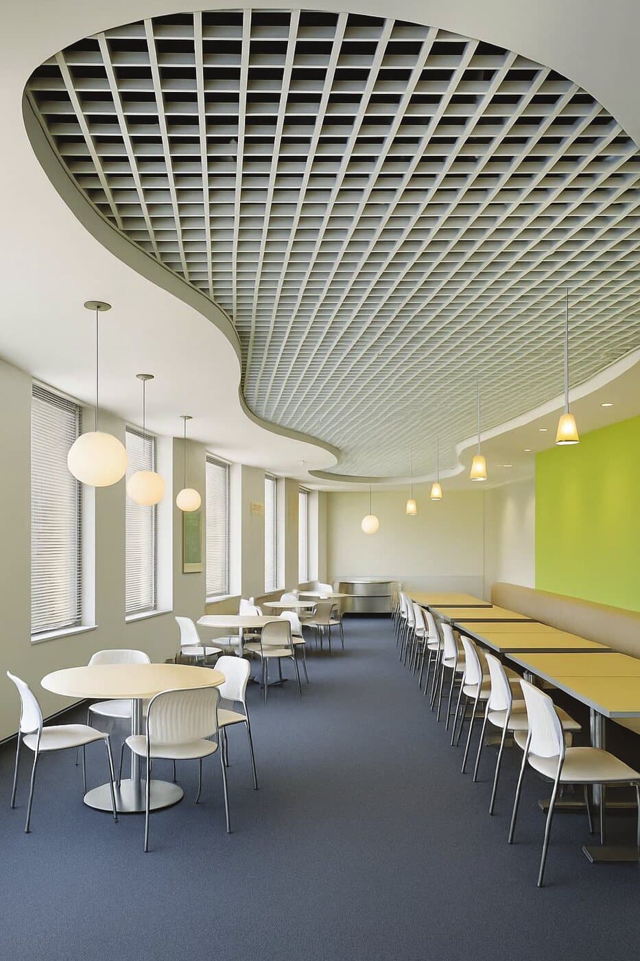 Cafeteria below a curved white open cell metal ceiling with pendant lighting